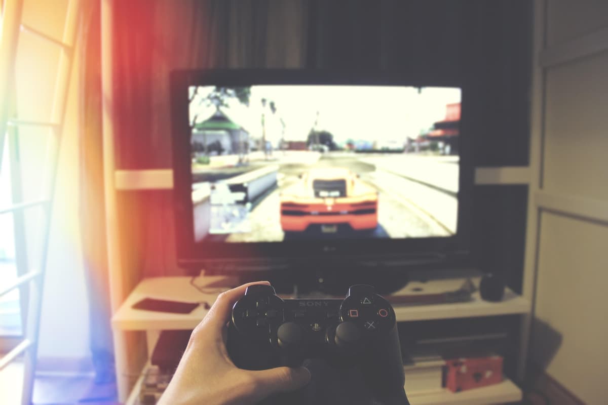 A hand holding a game controller in front of a television showing a driving game