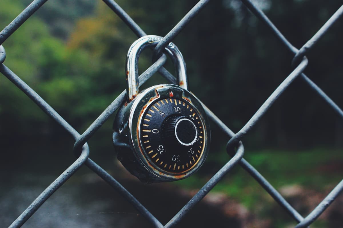 A combination padlock closed through a chain-link fence, with the numbered dial in focus